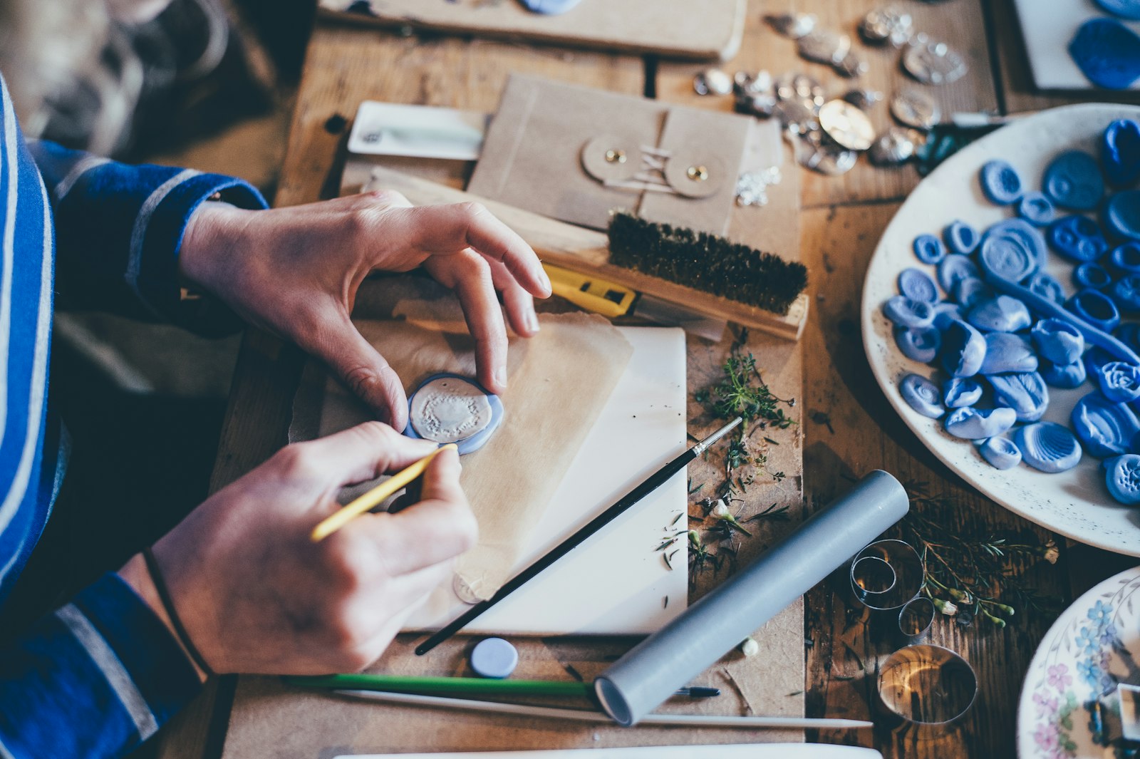hands working with craft materials at a cluttered workbench