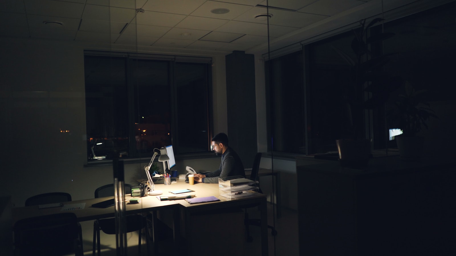 a man working alone at a dimly lit office desk late at night